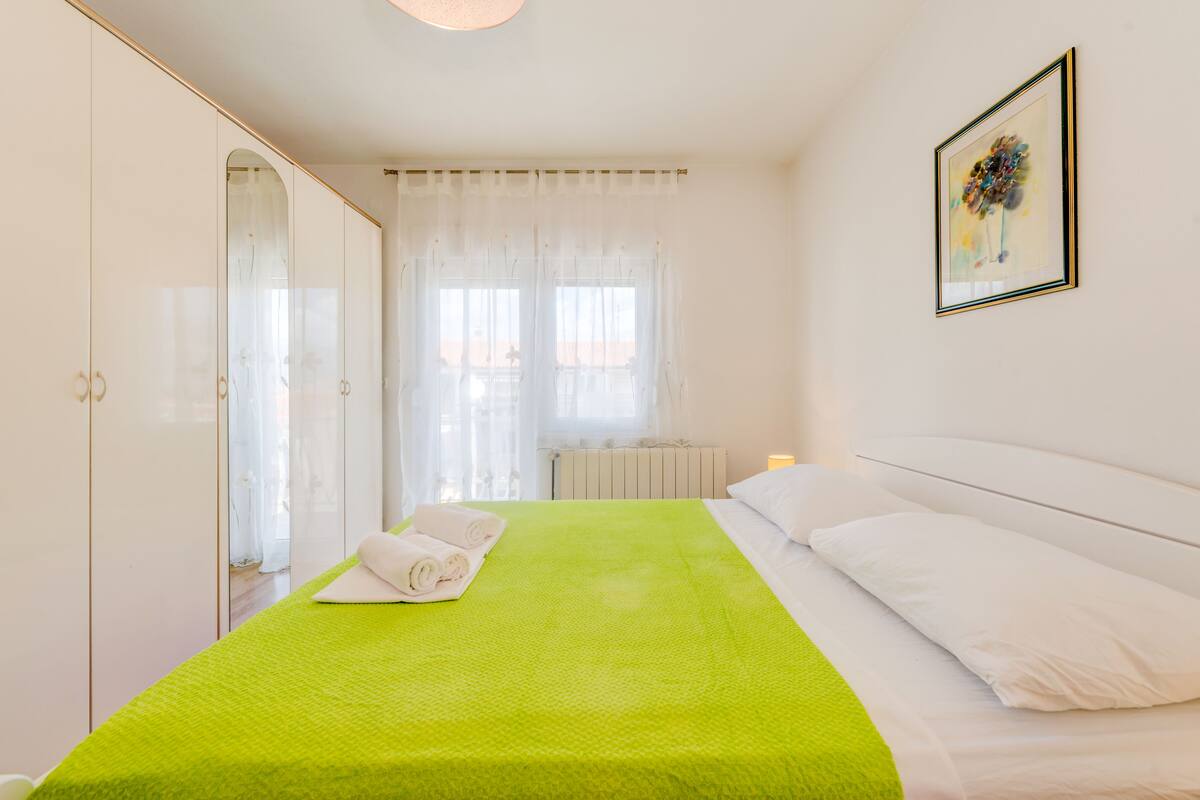 A hotel room with a bed, a large mirror, and a window with sheer curtains.