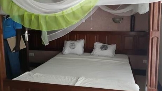 A single bed with a white bedspread and two pillows, a wooden headboard, and a green and white canopy. - Solomon Castle Hotel Mombasa (Mombasa)