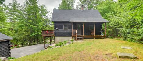 A log cabin with a porch, surrounded by lush greenery and trees.