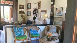 A cozy room with wicker furniture, a ship's wheel decoration, and framed pictures on the wall. - Beautiful and Comfortable House for up to 15 People in Arraial do Cabo (Location: Vacation Rental) (Arraial do Cabo)