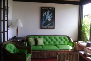 A green upholstered sofa with a cushion, a wicker chair, and a framed artwork on the wall.