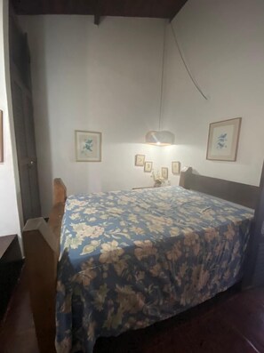 A bedroom with a bed, a nightstand, and a hanging light fixture.