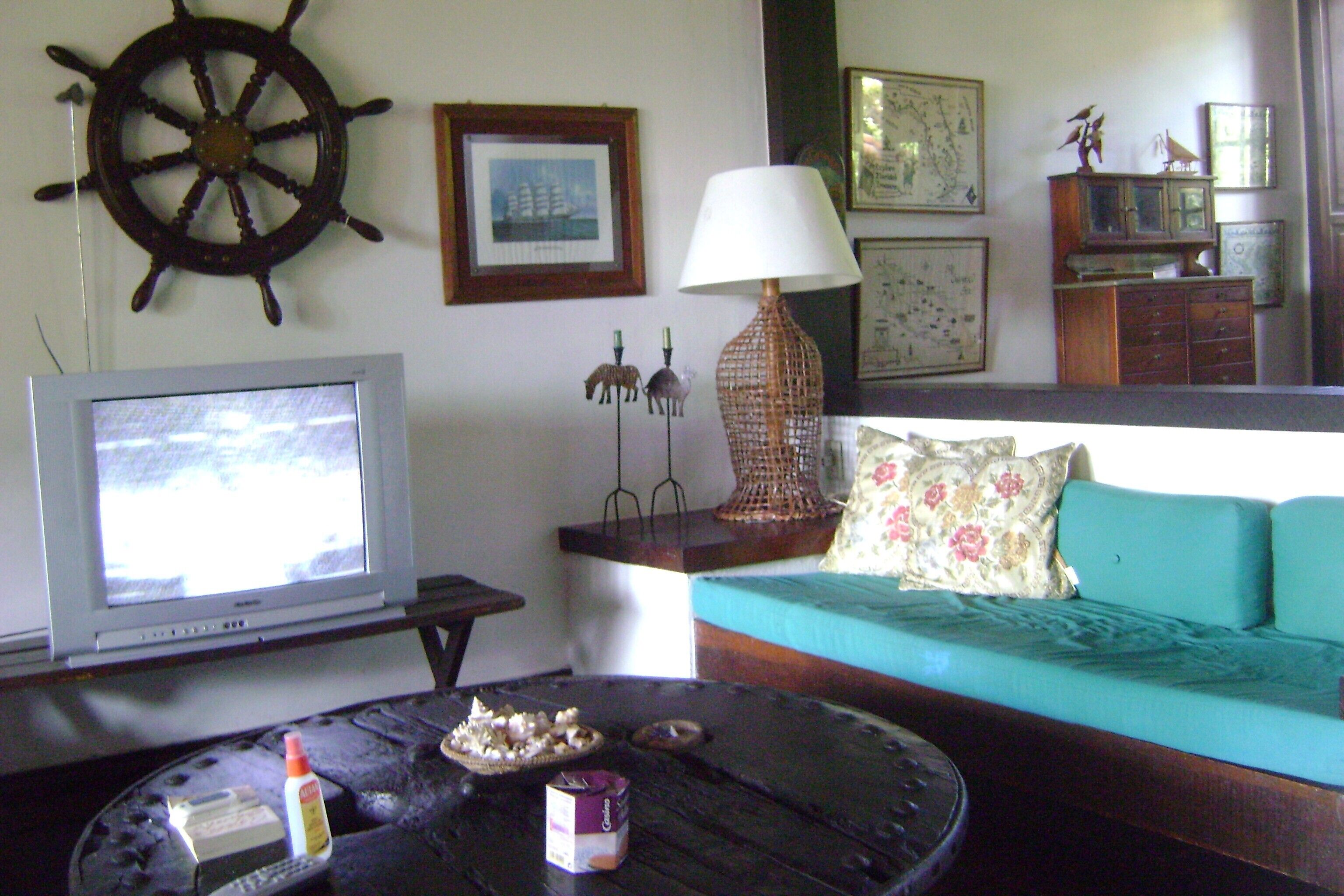 A living room with a television, a round coffee table, a sofa, and a wall-mounted ship's wheel.