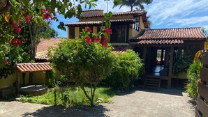 A courtyard with a tiled floor, surrounded by lush greenery and flowering plants. - Beautiful and Comfortable House for up to 15 People in Arraial do Cabo (Location: Vacation Rental) (Arraial do Cabo)