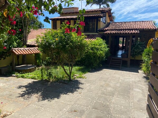 A courtyard with a tiled floor, surrounded by lush greenery and flowering plants.