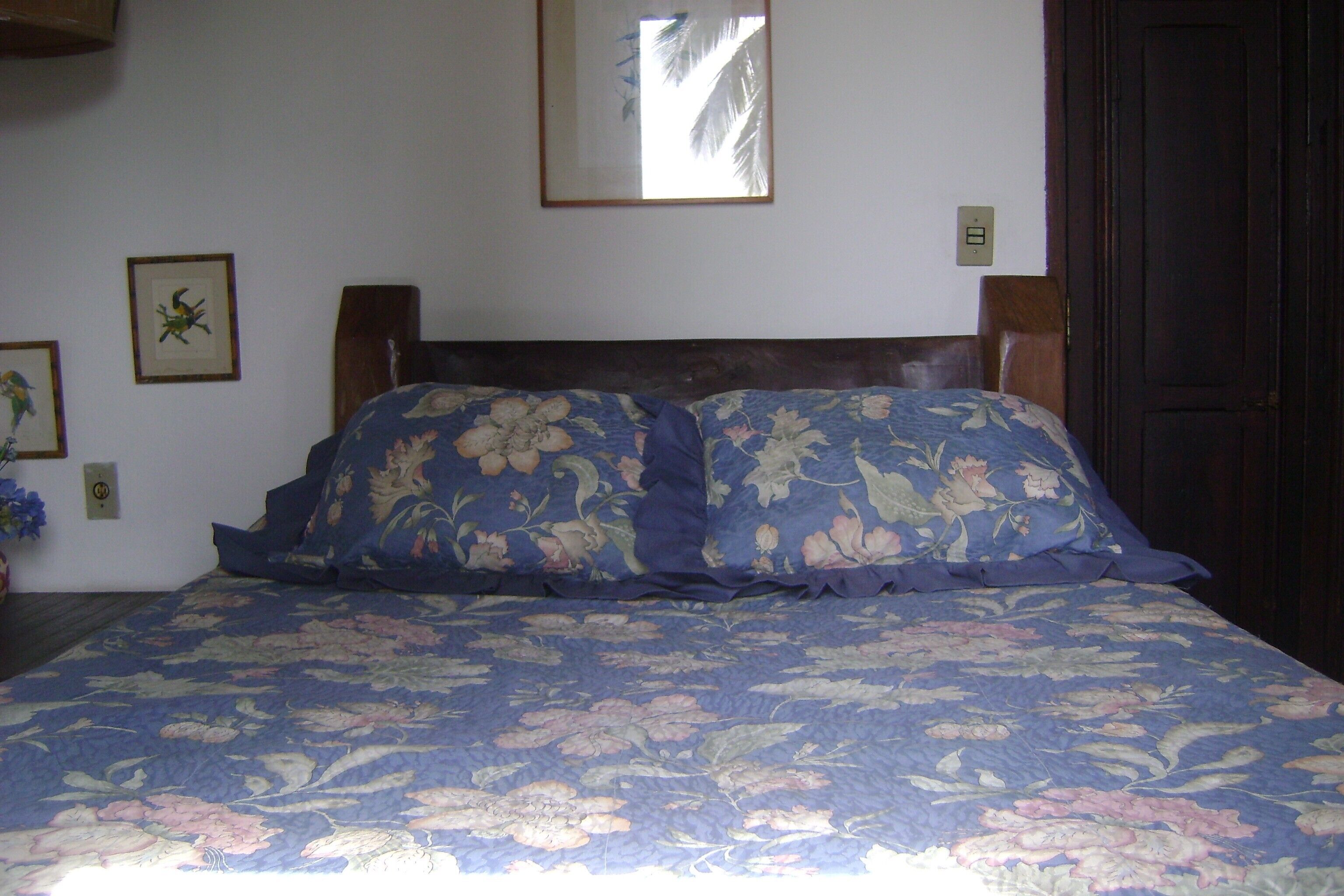 A bedroom with a floral bedspread, a wooden headboard, and a wall-mounted mirror.