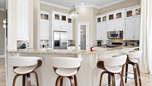 A modern kitchen with white cabinets, a granite countertop, and a central island with bar stools. - Themed Games Room | Kids Bedrooms | Private Pool with Summer Kitchen | Golf Course Views (Kissimmee)