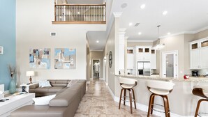 A modern kitchen with white cabinets, a stainless steel refrigerator, and a bar area with stools. - Themed Games Room | Kids Bedrooms | Private Pool with Summer Kitchen | Golf Course Views (Kissimmee)