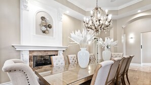 A dining room with a glass-top table, upholstered chairs, a white vase, and a chandelier. - Themed Games Room | Kids Bedrooms | Private Pool with Summer Kitchen | Golf Course Views (Kissimmee)
