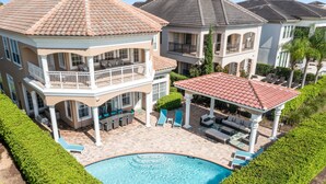 A two-story house with a swimming pool, outdoor seating, and a covered patio area. - Themed Games Room | Kids Bedrooms | Private Pool with Summer Kitchen | Golf Course Views (Kissimmee)