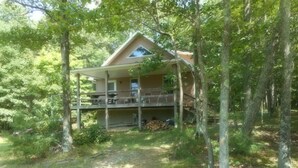A two-story cabin with a deck, surrounded by trees. - Mountain views, total seclusion Southern Bedford County, PA - Big Discounts! (Clearville)