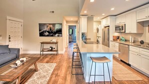 A modern kitchen with white cabinets, a central island, bar stools, and a dining area with a sofa and coffee table.