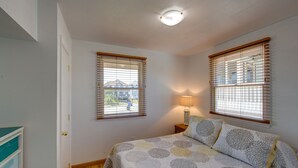Un dormitorio con dos ventanas, una cama con colcha estampada, una lámpara de noche y vistas al exterior.