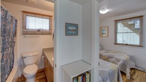 Un dormitorio compacto con dos camas, un baño pequeño con inodoro y una ventana con persianas.
