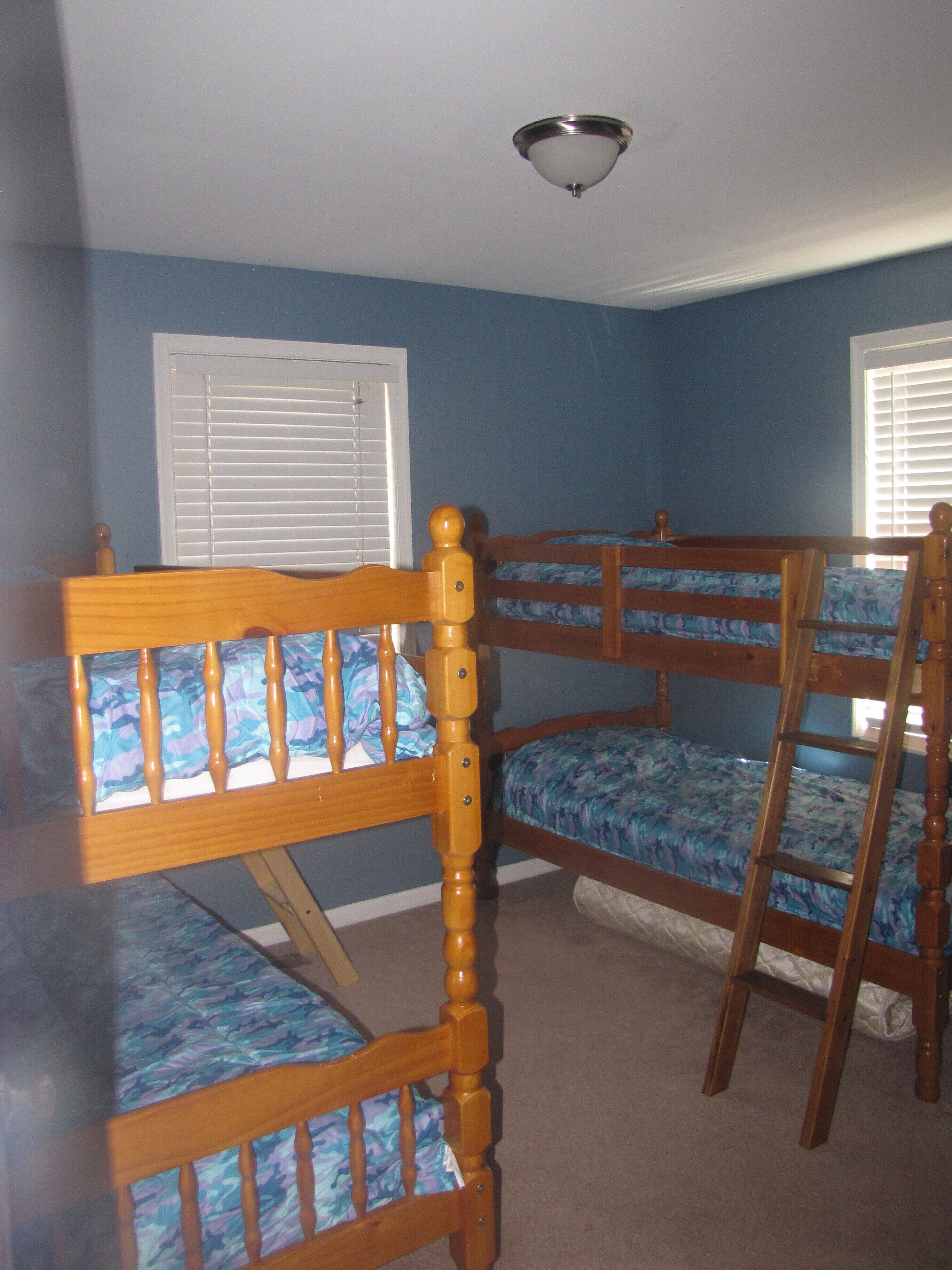 A room with bunk beds, a ceiling fan, and windows with blinds.