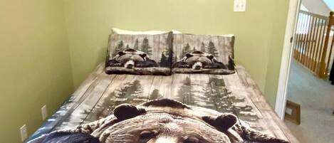 Una cama con una colcha de temática de oso en una habitación con paredes verdes y una escalera visible.