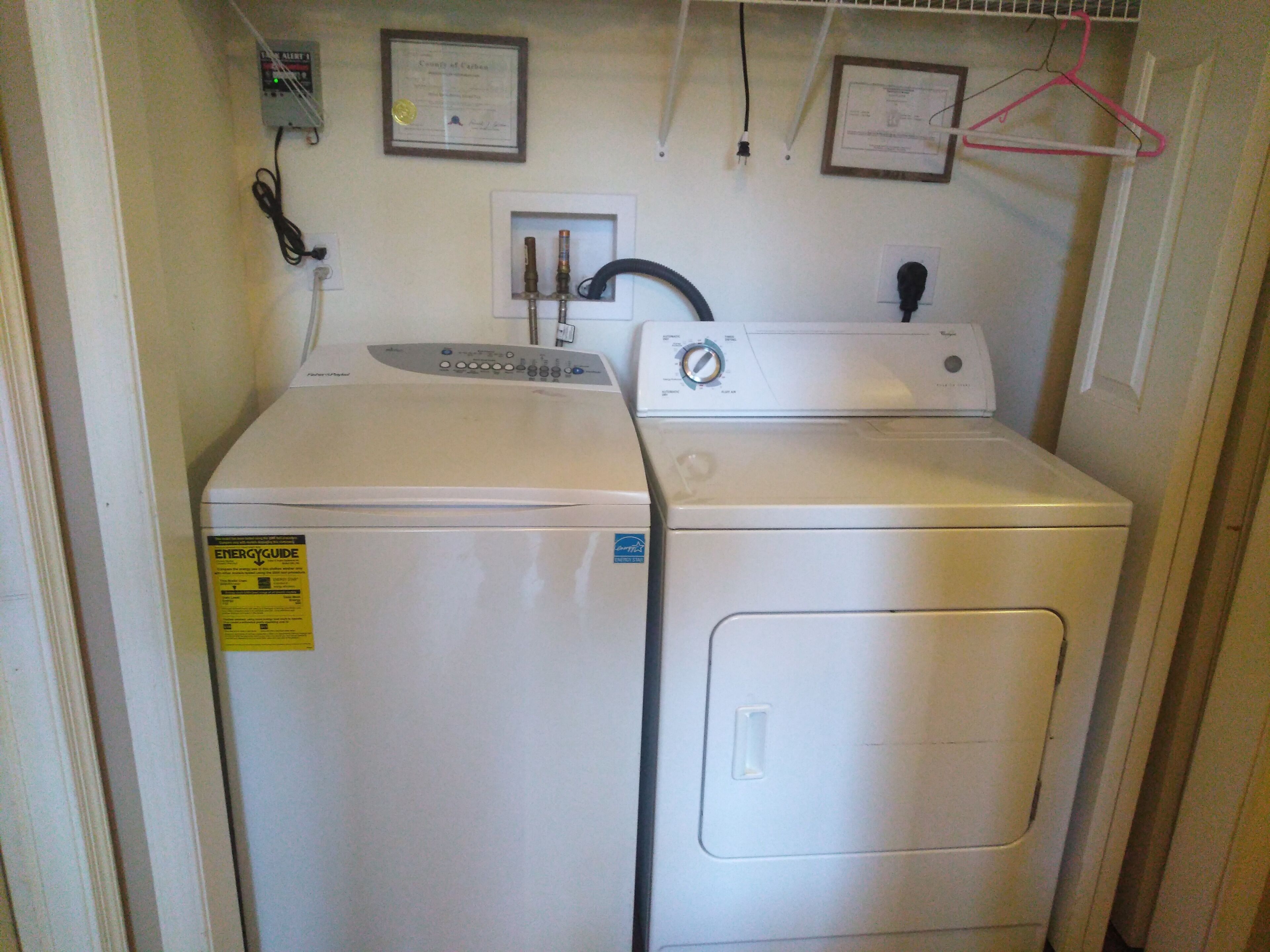 Een wasserette met een voorlader wasmachine en droger, een gasmeter en een certificaat aan de muur.