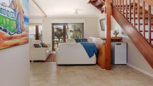 Ein modernes Wohnzimmer mit einem weißen Sofa, einer kleinen Küchenzeile und einer Holztreppe.