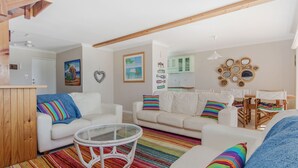 Ein gemütliches Wohnzimmer mit zwei weißen Sofas, einem Glastisch und farbenfrohen Streifen Teppichen.
