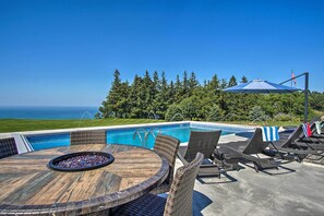A poolside area with a view of the ocean, a fire pit, and lounge chairs.