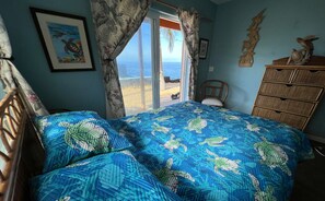 Een slaapkamer met een bed, een dressoir, een stoel en uitzicht op het strand door een schuifdeur.