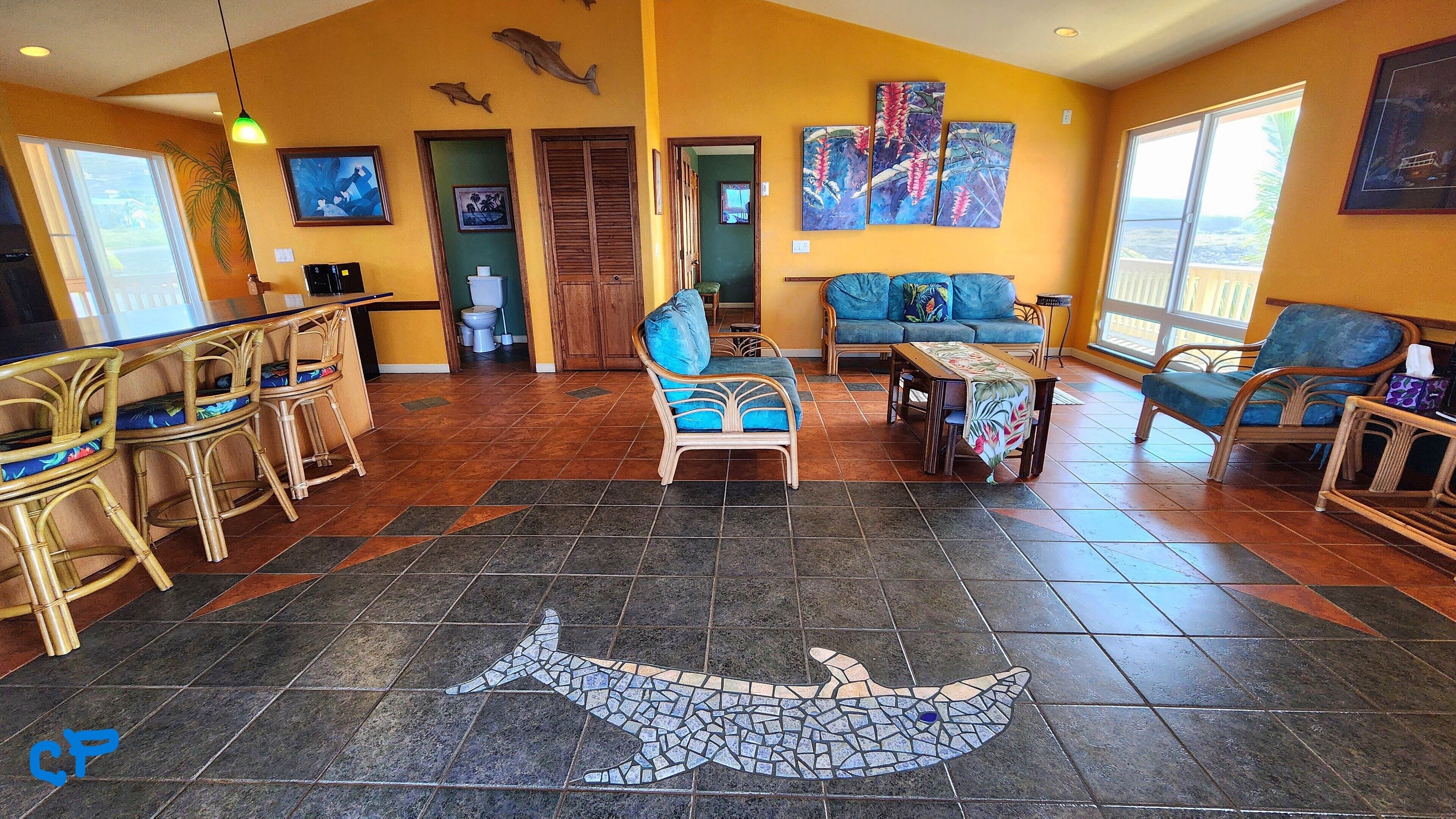 A spacious living area with a large shark mosaic on the floor, a bar area with wicker furniture, and a view through the door to the outside.