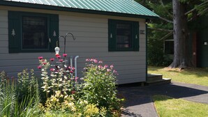 A small building with a green roof and white siding, a number '126' on the side, and a small porch with steps leading up to it.