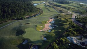 Vista aérea de un campo de golf con varios hoyos, búnkeres de arena y un obstáculo acuático.