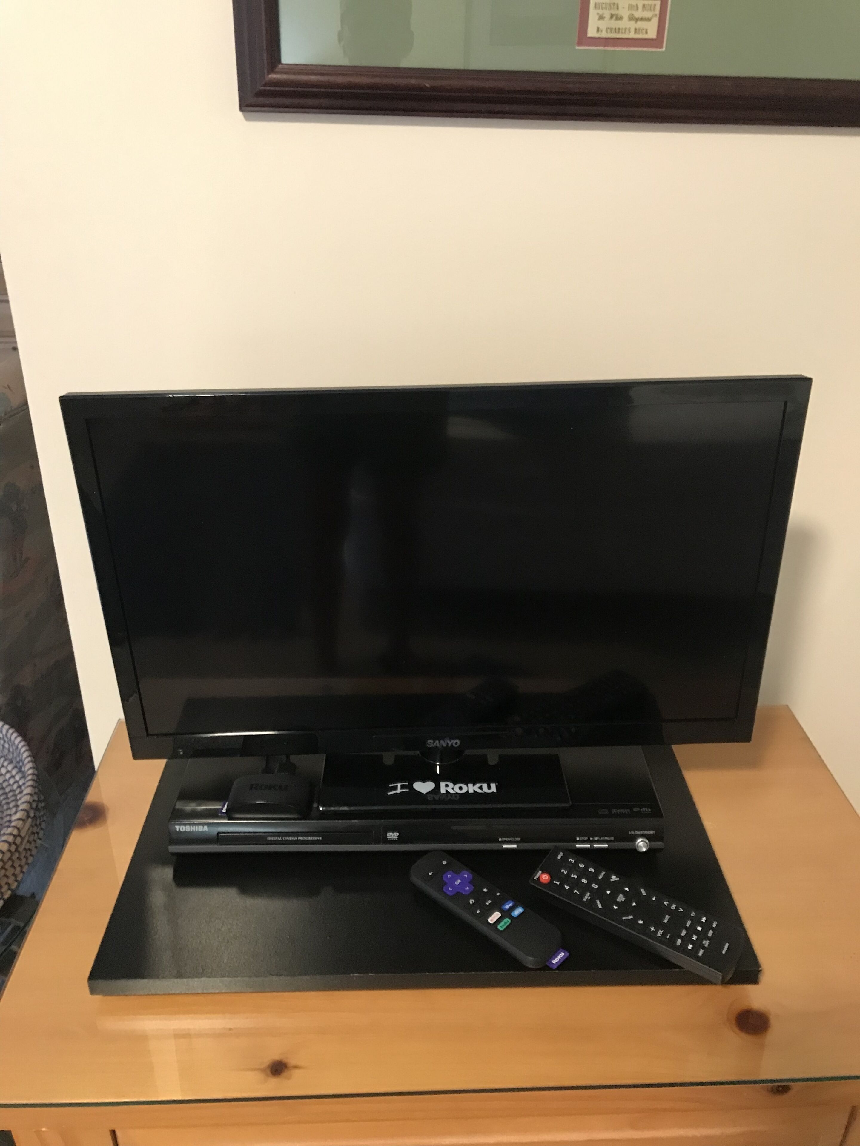 A television on a wooden stand with a remote control and a cable box labeled "I ♥ Roku".