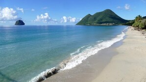 A beach with clear turquoise water, a sandy shore, and a mountain in the background. - pool, 100 m from the beach, sea, relaxation and standing facing Diamond Rock (Le Carbet)