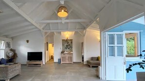 A spacious living area with a high ceiling, a television, a wicker sofa, and a dining area with a table and chairs. - pool, 100 m from the beach, sea, relaxation and standing facing Diamond Rock (Le Carbet)