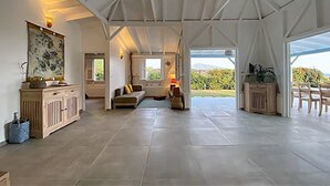 A spacious living area with a high ceiling, a large window, and a view of the outdoors. - pool, 100 m from the beach, sea, relaxation and standing facing Diamond Rock (Le Carbet)