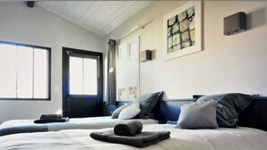 Een hotelkamer met twee bedden, een groot raam, een deur en een kunstwerk aan de muur.