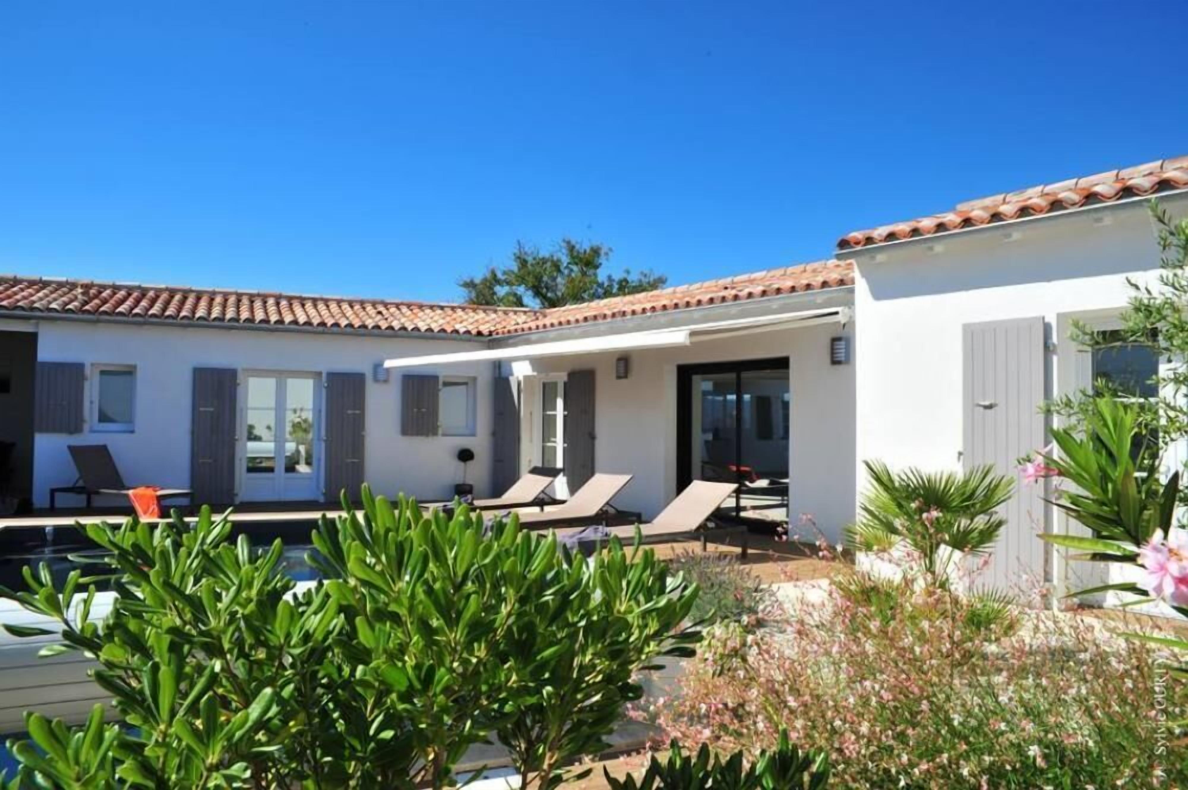 A modern villa with a swimming pool, sun loungers, and a garden area.