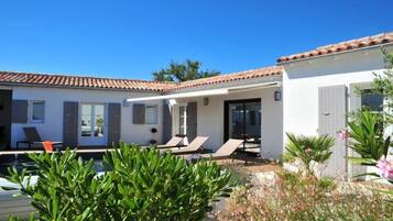 A modern villa with a swimming pool, sun loungers, and a garden area.