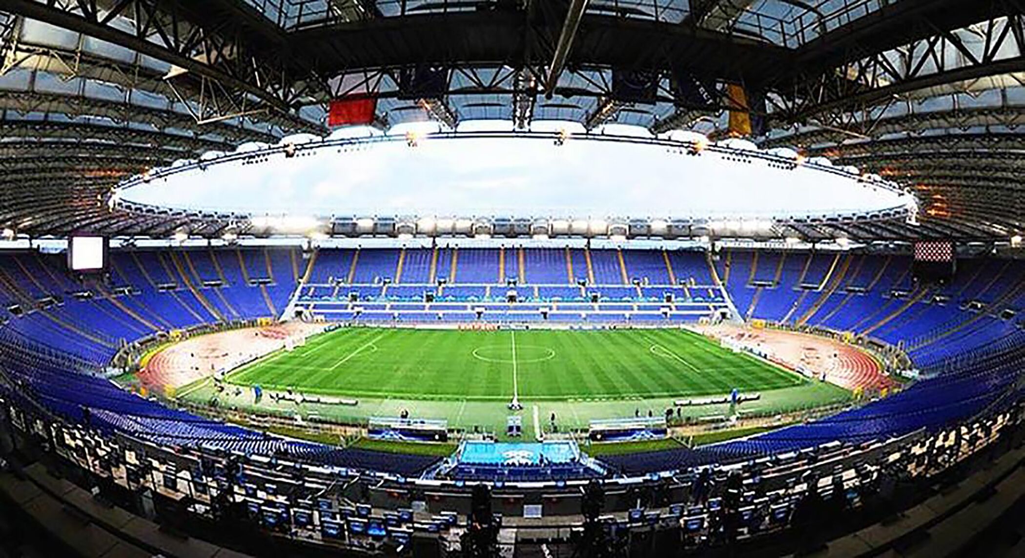 A large stadium with multiple tiers of seating, a central field, and a roof structure.
