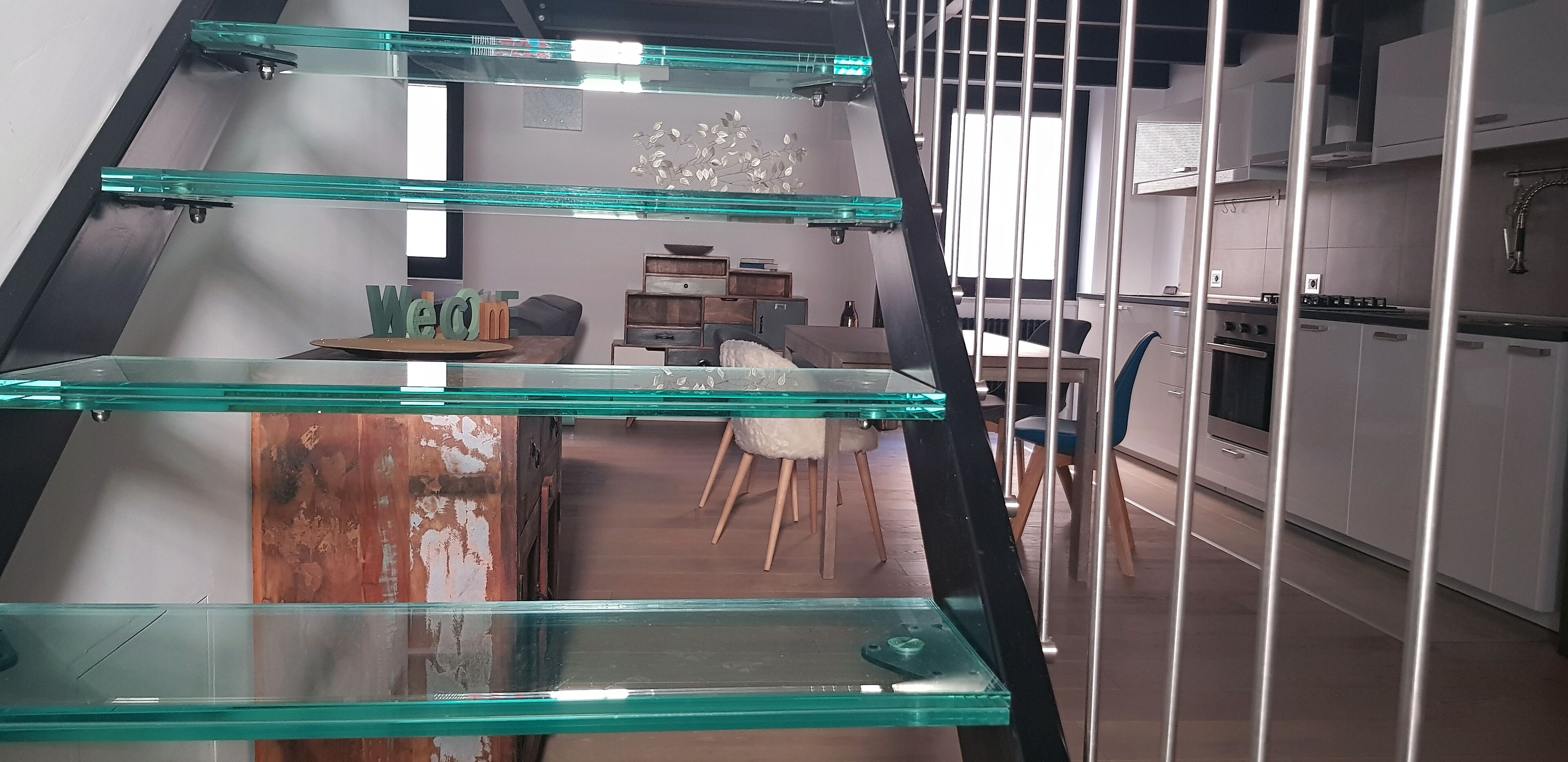 Une cuisine moderne dotée d’appareils électroménagers en acier inoxydable, un coin repas avec une table en verre et un escalier avec des rampes en verre.