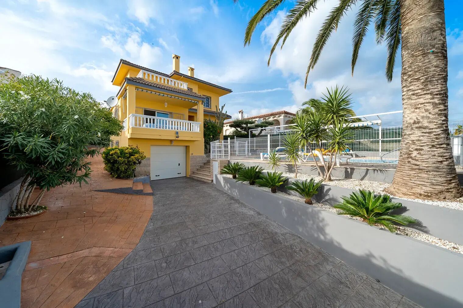 A yellow two-story house with a balcony, a garage, and a swimming pool area.