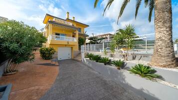 A yellow two-story house with a balcony, a garage, and a swimming pool area.