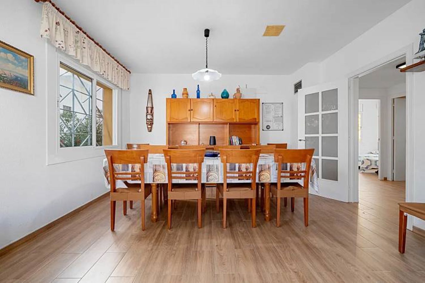 A dining area with a wooden table and chairs, a ceiling light, and a window with curtains.