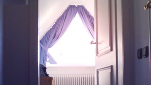 Un pasillo estrecho que conduce a una habitación con techo inclinado y una ventana con cortinas moradas.