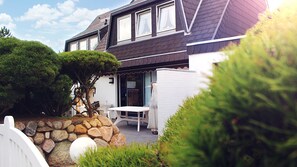 A two-story house with a stone wall, a white fence, and a patio with a table and chairs. - Generous, friendly DHH with terrace and garden in the heart of Westerland (Westerland)