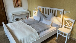 Una cama bien tendida con un cabecero blanco, una mesita de noche con una lámpara y una silla.