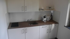Una cocina pequeña con armarios blancos, una encimera de madera, un lavabo y una tetera.