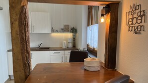 Una mesa de madera con sillas, una pared blanca con un letrero y una cocina al fondo.