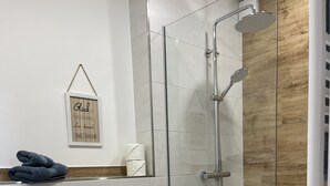Un baño moderno con cabina de ducha de vidrio, inodoro blanco, lavamanos y un cubo de basura.