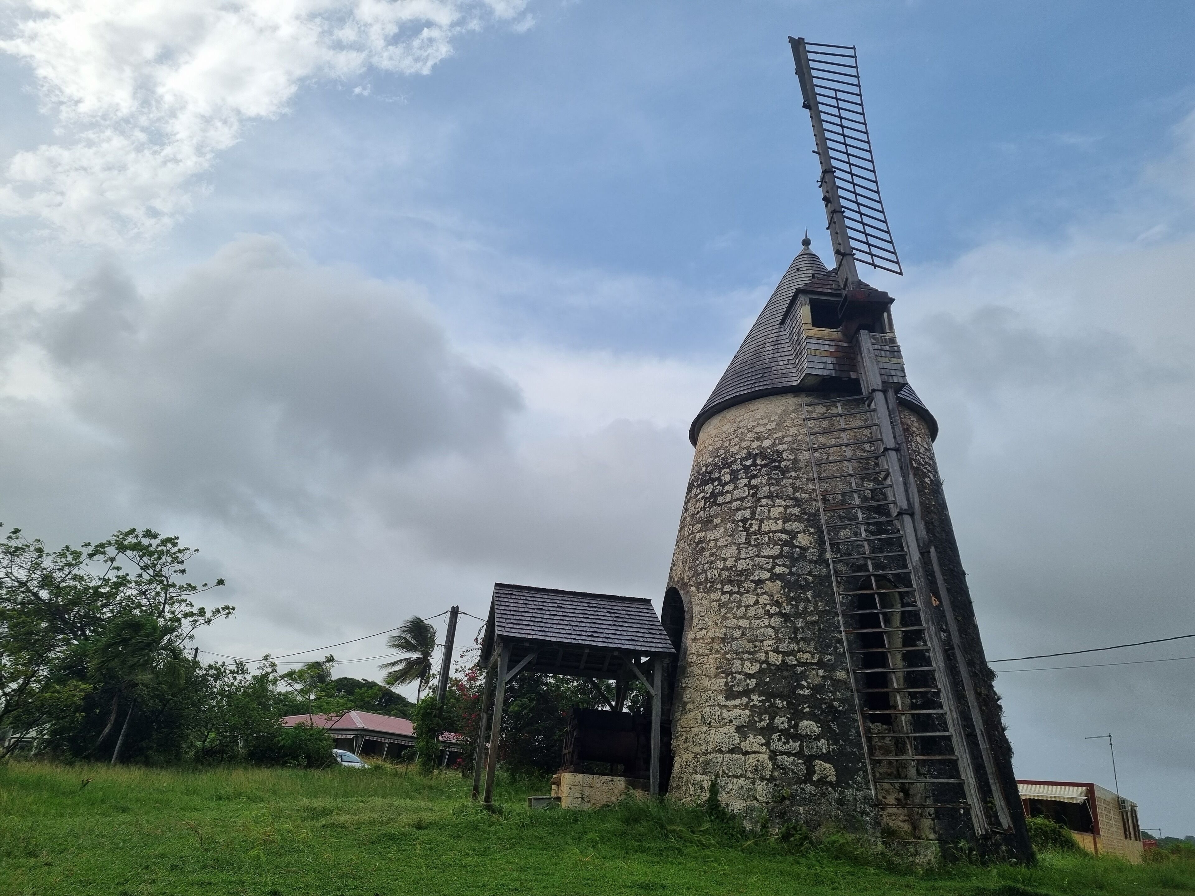Een stenen windmolen met een metalen ladder en een metalen dwarsbalk.