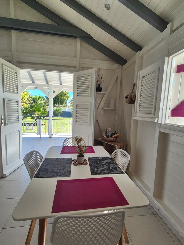 A dining area with a table set for two, white walls, and a view of the outdoors.