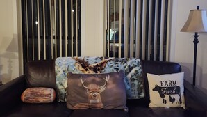 A dark leather sofa with three decorative pillows, one with a deer image, another with a farm animal silhouette, and a third with a patterned design.
