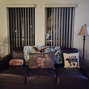 A dark leather sofa with three decorative pillows, one with a deer image, another with a farm animal silhouette, and a third with a patterned design.